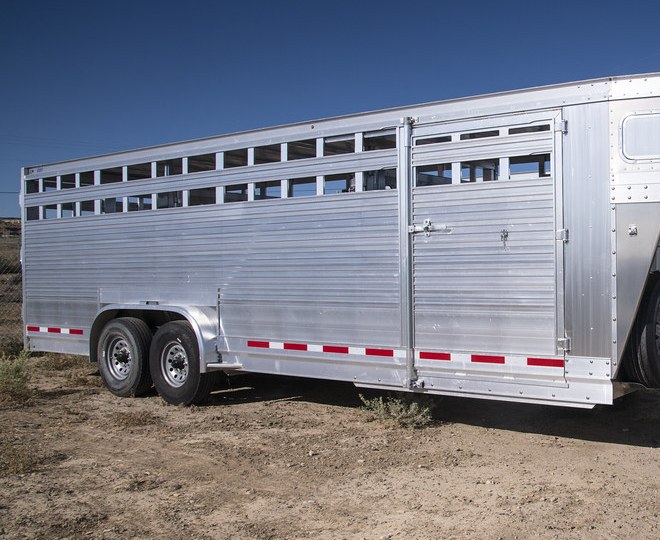 PLACEHOLDER: an aluminium livestock trailer in side elevation, slat sides above solid lower panels, tandem axles, standing on bare ground.
